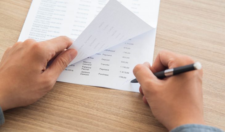 Close-up of male hands signing accounting documents. Businessman sitting at table in office